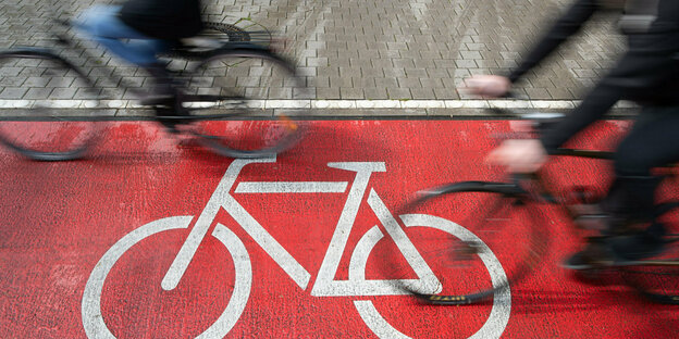 Radfahrer fahren auf einem roten Radweg, auf den ein Fahrrad in weißer Farbe aufgemalt ist