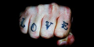 Eine geballte Faust, auf die vier Finger ist das Wort "LOVE" tätowiert