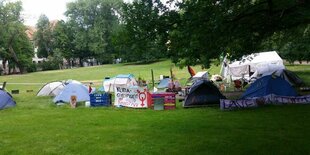 Ein paar Zelte, Pavillons und Banner unter Bäumen auf einer Wiese