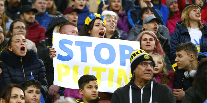 Eine weinende Frau im Fussballstadionm it einem Schild: Stop Putin