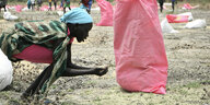 Eine Frau sammelt im Südsudan Hirse vom Boden auf, die in rosa Säcken vom Welternährungsprogramm (WFP) abgeworfen wurden