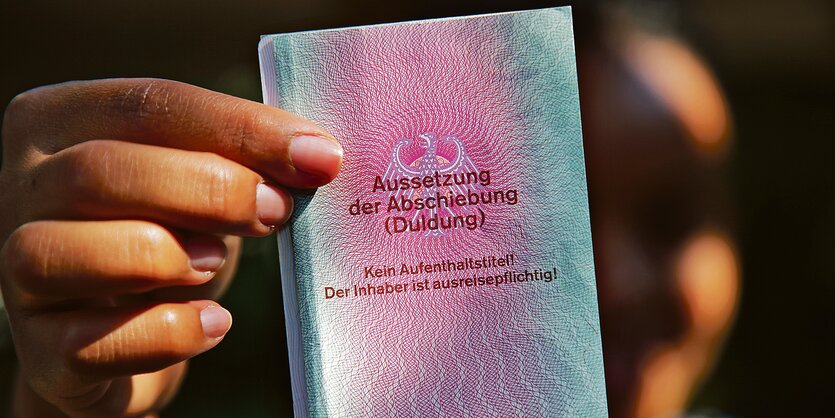 Ein Mensch hält ein Dokument in der Hand auf dem steht: "Aussetzung der Abschiebung".