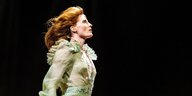 Florence Welch geht in einem weißen Kleid mit Mikrofon energisch über die Bühne