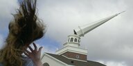 Einer Frau stehen vor einem schiefen, abgeknickten Kirchturm in den USA die Haare zu Berge