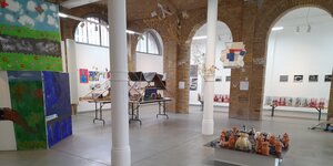 Raumansicht der Ausstellung "Brücken Beats Berlin": Rechts im Bild ist eine Plattform mit Eulen aus Keramik zu sehen, darüber Wandarbeiten aus Stoff und Bambusstäben