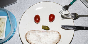 Ein Gesicht aus Tomaten, einer Gurke und einem Butterbrot, die auf einem Teller liegen