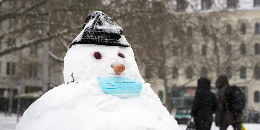 Schneemann im Park mit Mütze und blauer medizinischer Maske