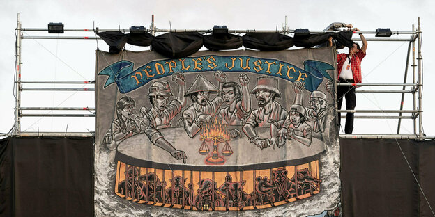 Ein Kunstwerk bei der Documenta in Kassel zeigt ein Banner mit mehreren Menschen mit erhobenen Fäusten und Tieren unter ihnen.