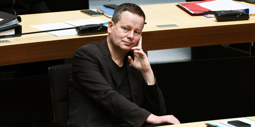 Klaus Lederer sitzt im Plenarsaal und stützt nachdenklich den Kopf in die Hand, guckt dabei aber aufrecht