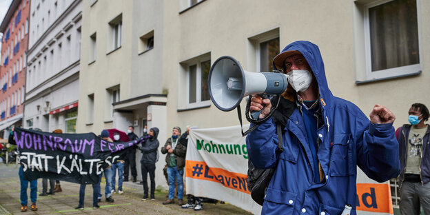 Ein Mann ruft bei der Besetzung der Habersaathstraße im Herbst 2020 etwas ins Megafon, hinter ihm stehen Demonstrant*innen mit Bannern gegen Obdachlosigkeit.