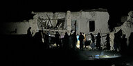 Umrisse von Menschen bei Nacht vor einer beleuchteten Ruine.
