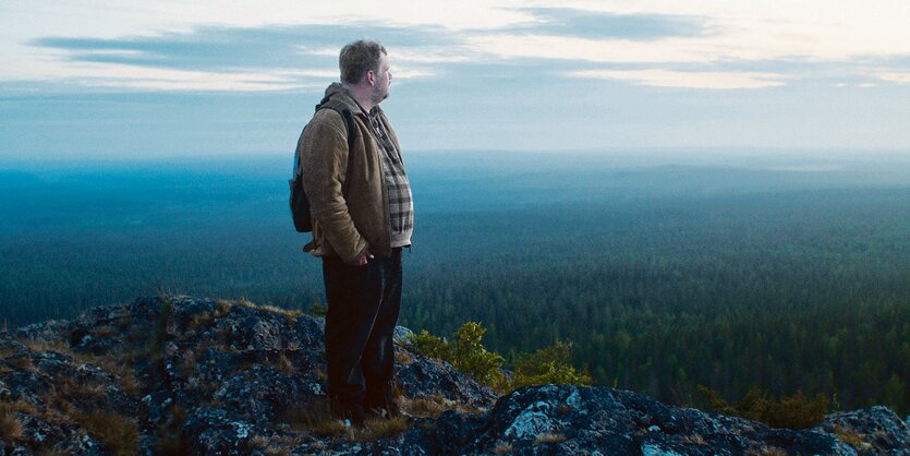 Daniel steht auf einer Anhöhe und blickt auf einen Wald, der sich unter ihm bis zum Horizont erstreckt.