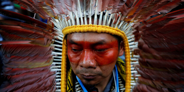 Ein indigener Mann mit Federschmuck nimmt an einem Protestmarsch zum Klimawandel teil