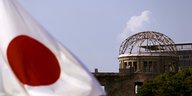 links im Vordergrund japanische Flagge, rechts dahinter Ruine in Hiroshima