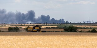 Schwarzer Rauch, im Vordergrund ein Mähdrescher auf einem Weizenfeld.