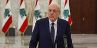 Ein Mann im Anzug steht an einem Mikrofon vor libanesischen Flaggen