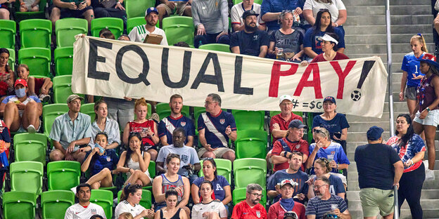 Fans mit einem Transparent mit der Aufschrift "Equal Pay!" im Stadion