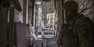 Soldate steht in einem zerstörten Gebäude und guckt aus dem fenster
