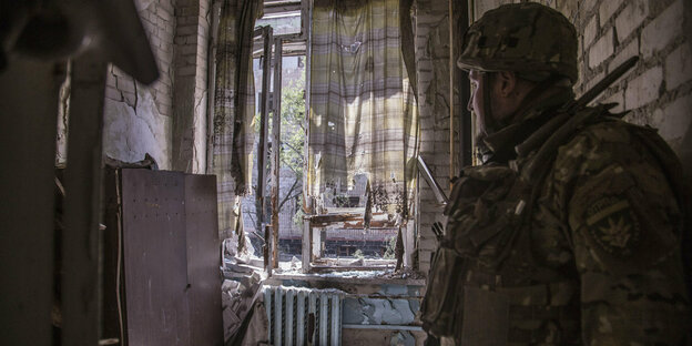 Soldate steht in einem zerstörten Gebäude und guckt aus dem fenster