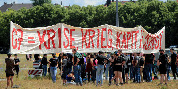 Demonstrant:innen hinter einem Transparent mit der roten Aufschrift "G7 = Krise, Krieg, Kapitalismus" Demonstrant:innen hinter einem Transparent mit der roten Aufschrift "G7 = Krise, Krieg, Kapitalismus"