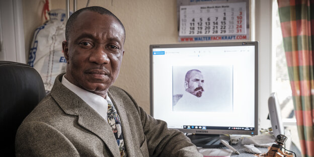 Ein Schwarzer Mann sitzt vor einem Computer-Bildschirm, auf dem ein Bild von seinem weißen Großvater zu sehen ist.