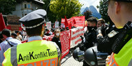 Polizist in gelber Weste mit der Aufschrift: Anti-Konflikt-Team vor Demonstranten in Elmau