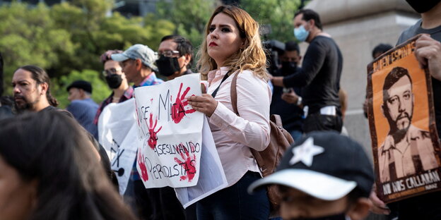 Eine Frau hält ein Plakat in der Hand, darauf sind blutige Handabdrücke erkennbar