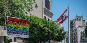 Eine aus regenbogenfarbenen Blumen gefertigte Plakatwand hängt neben einer libanesischen Fahne