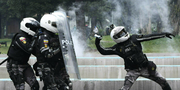 ein Polizist wirft eine Tränengasgranate, hinter ihm schützen sich drei Kollegen hinter ihren Schilden