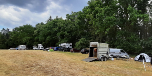 Autos, ein Hänger und ein Zelt stehen auf einem Feld