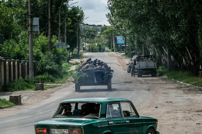 Autos und Panzer fahren durch eine unasphalitierte Straße