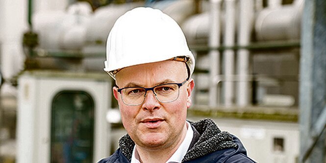 Tobias Goldschmidt mit einem Schutzhelm vor einer Industrieanlage.