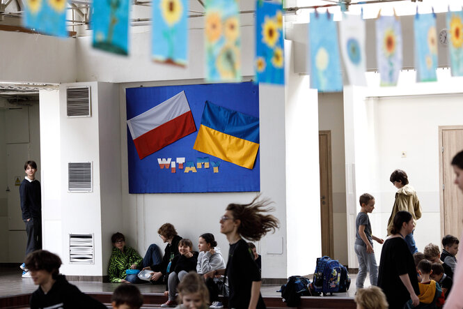 Eine ukrainische und eine polnische Flagge hängen in einem Schulflur, viele Kinder im Bild