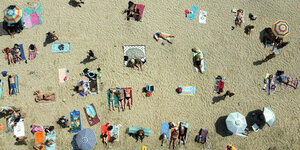 Menschen in Badekleidung an einem sandigen Strand von oben aufgenommen