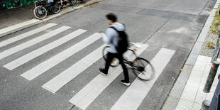 Ein Mann schiebt sein Fahrrad über einen Zebrastreifen