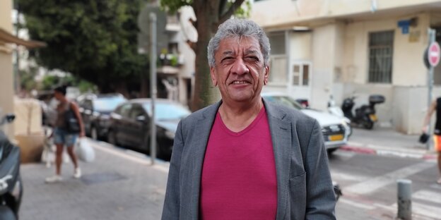 Najem Wali mit lila T-Shirt und Anzugsjacke schaut in die Kamera auf eiiner Straße in Tel Aviv
