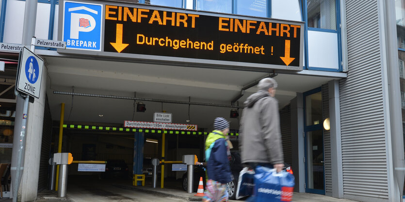 Die Einfahrt zum Parkhaus Mitte in Bremen in der Pelzerstraße; zwei Menschen mit Einkaufstüten laufen vorbei, an einer Leuchtanzeige über der Einfahrt steht "durchgehend geöffnet"