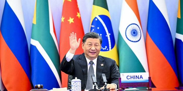 Chinas Präsident Xi Jinping mit erhobener Hand vor mehreren Landesflaggen