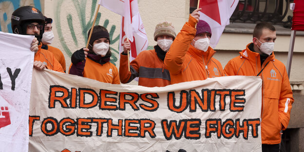 Lieferando Arbeiter:innen in orangen Jacken mit der Aufschrift: Riders Unite, Together We Fight