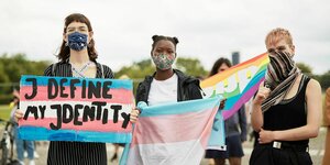 3 Personen mit Transgender-Flagge demonstrieren vor dem Reichstag in Berlin