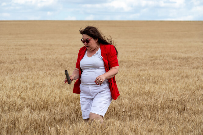 Eine Frau steht in einem Feld und hält eine Patronenhülse in ihrer Hand