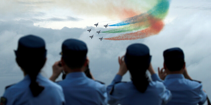 Flugzeuge fliegen in Formation und zeihen bunte Rauchschwaden hinter sich her