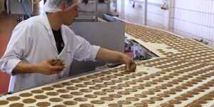 Ein Arbeiter prüft Lebkuchen auf einem Fließband