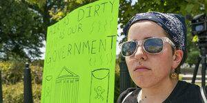 Eine Frau mit Stirnband hält ein Plakat hoch. Darauf steht: "Unsere Luft ist so schmutzig wie unsere Regierung"