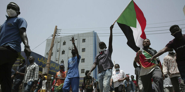 Menschen protestieren mit einer sudanesischen Fahne