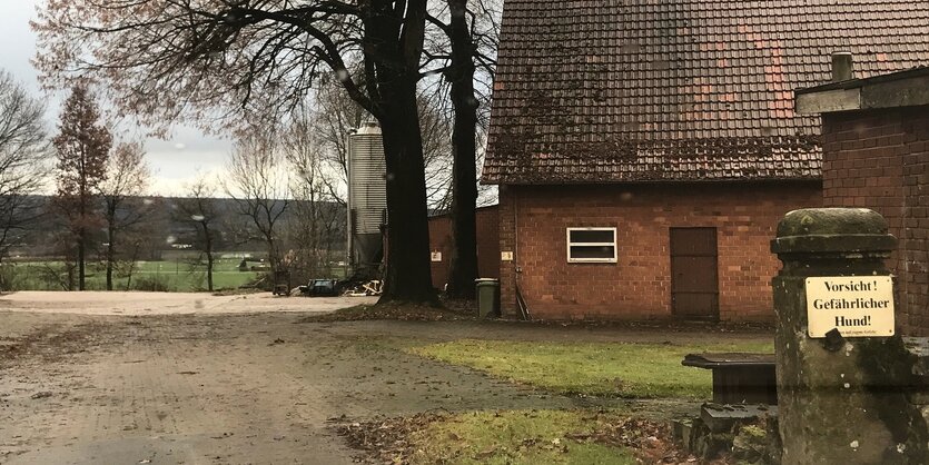 Ein Backsteingebäude mit entlaubten Bäumen und einem Schild: Vorsicht gefährlicher Hund