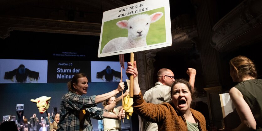 Viele Schauspielerinnen und Schauspieler spielen eine Protestszene. Auf einem Plakat steht: Wir sind kein Wolfsfutter