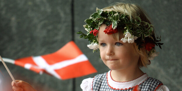 ein Mädchen in Tracht und mit Efeukranz hält eine dänische Fahne