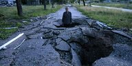 Ein Mann steht in einem Krater auf einer asphaltierten Straße, nur sein Oberkörper ragt heraus.