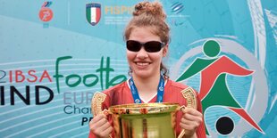 Thoya Küster mit dunkler Sonnenbrille hält an beiden Henkelen einen riesigen Pokal